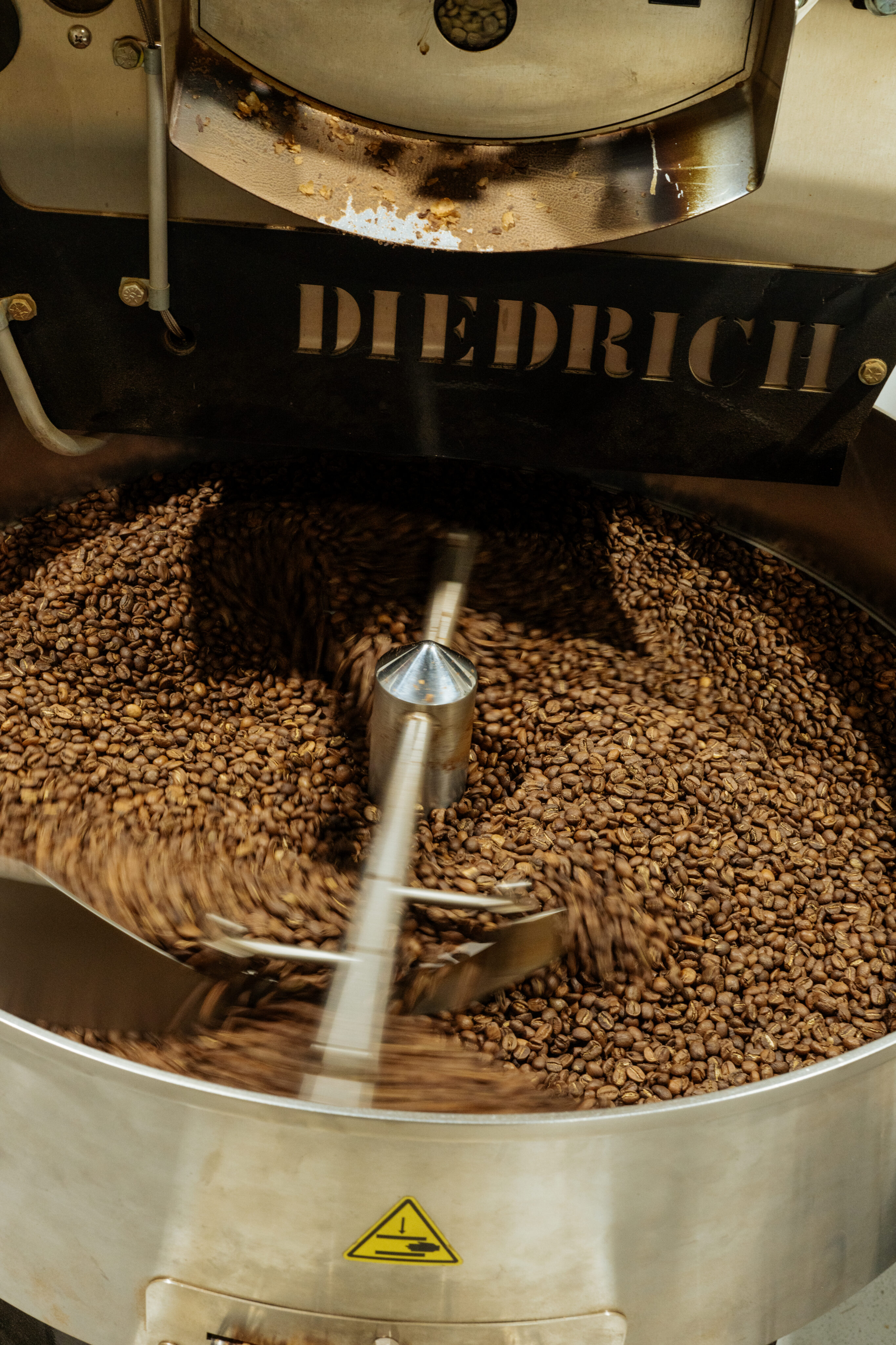 A coffee roasting machine with the brand name "Diedrich" processes a batch of brown coffee beans in motion inside a metal drum at Lamppost Coffee, bringing specialty coffee to life for every coffee shop enthusiast. - Lamppost Coffee